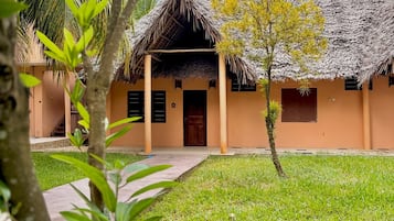 Un bâtiment à toit de chaume, doté d’une entrée pavée et d’un petit arbre au premier plan.