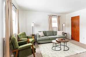 Un salon comprenant un canapé, deux fauteuils, une table basse et une porte.