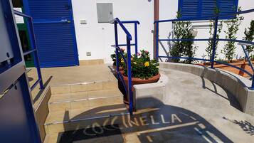 A set of outdoor stairs leading to a building entrance with a blue door and a sign reading 'Cocinella'.