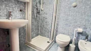 A bathroom with a glass-enclosed shower, a sink, a toilet, and a bidet.