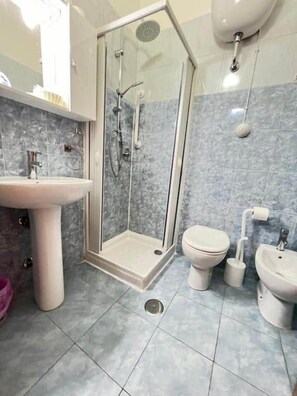 Un baño con ducha de vidrio, lavamanos, inodoro y bidé.