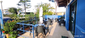 An outdoor patio area with tables and chairs, a blue railing, and potted plants.