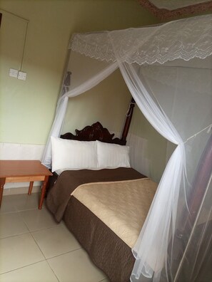 A single bed with a canopy, a wooden nightstand, and a wall socket. - New Honest Suites Mbarara (Mbarara)