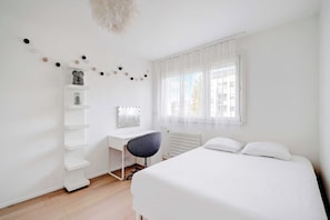 A minimalist bedroom with a bed, a desk with a chair, and a window with curtains. - Spacious Apartment- 3br/6p - Charenton (Charenton-le-Pont)