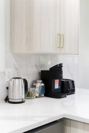 A kitchen with white cabinets, a kettle, a coffee maker, and a toaster on the counter.