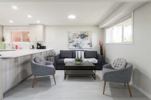 A modern living room with a sofa, two armchairs, a coffee table, and a kitchen area with a countertop and cabinets.