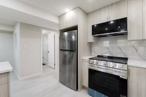 A modern kitchen with stainless steel appliances, a black oven, and light-colored cabinetry.