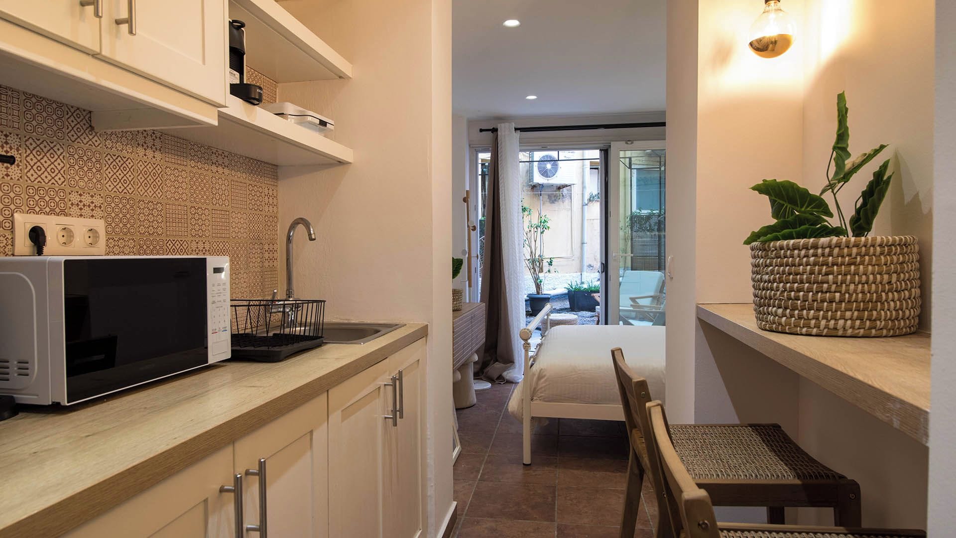 A compact kitchen with a microwave, a sink, and a window leading to a balcony.
