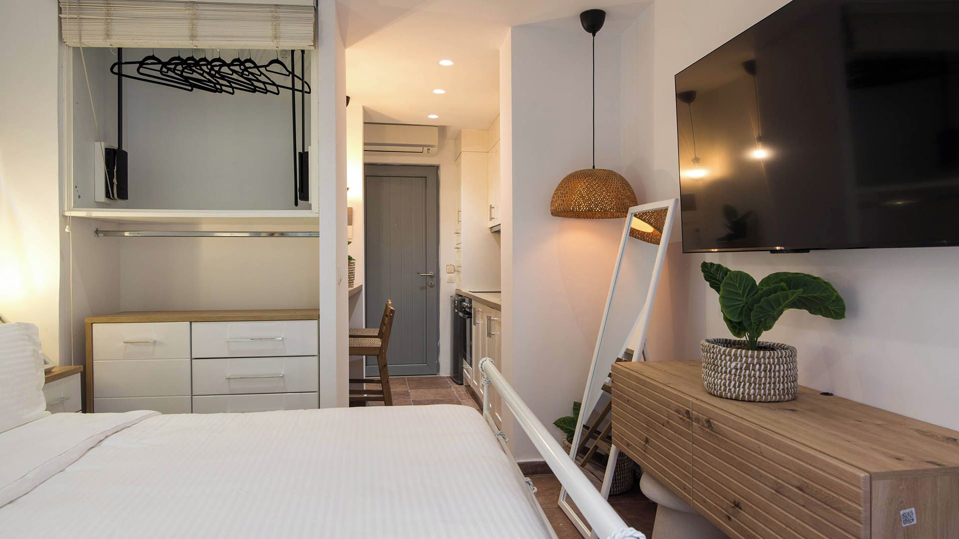 A bedroom with a bed, a dresser, a mirror, a hanging light fixture, and a potted plant.