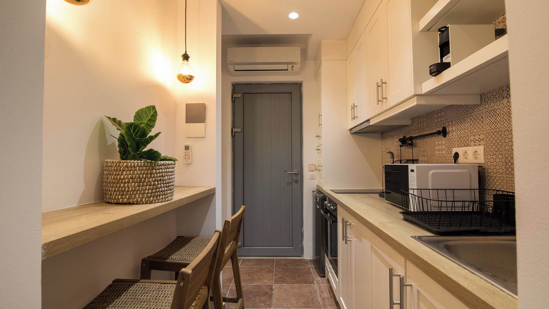 A compact kitchen with a built-in dishwasher, a small dining area with a bench, and a potted plant.