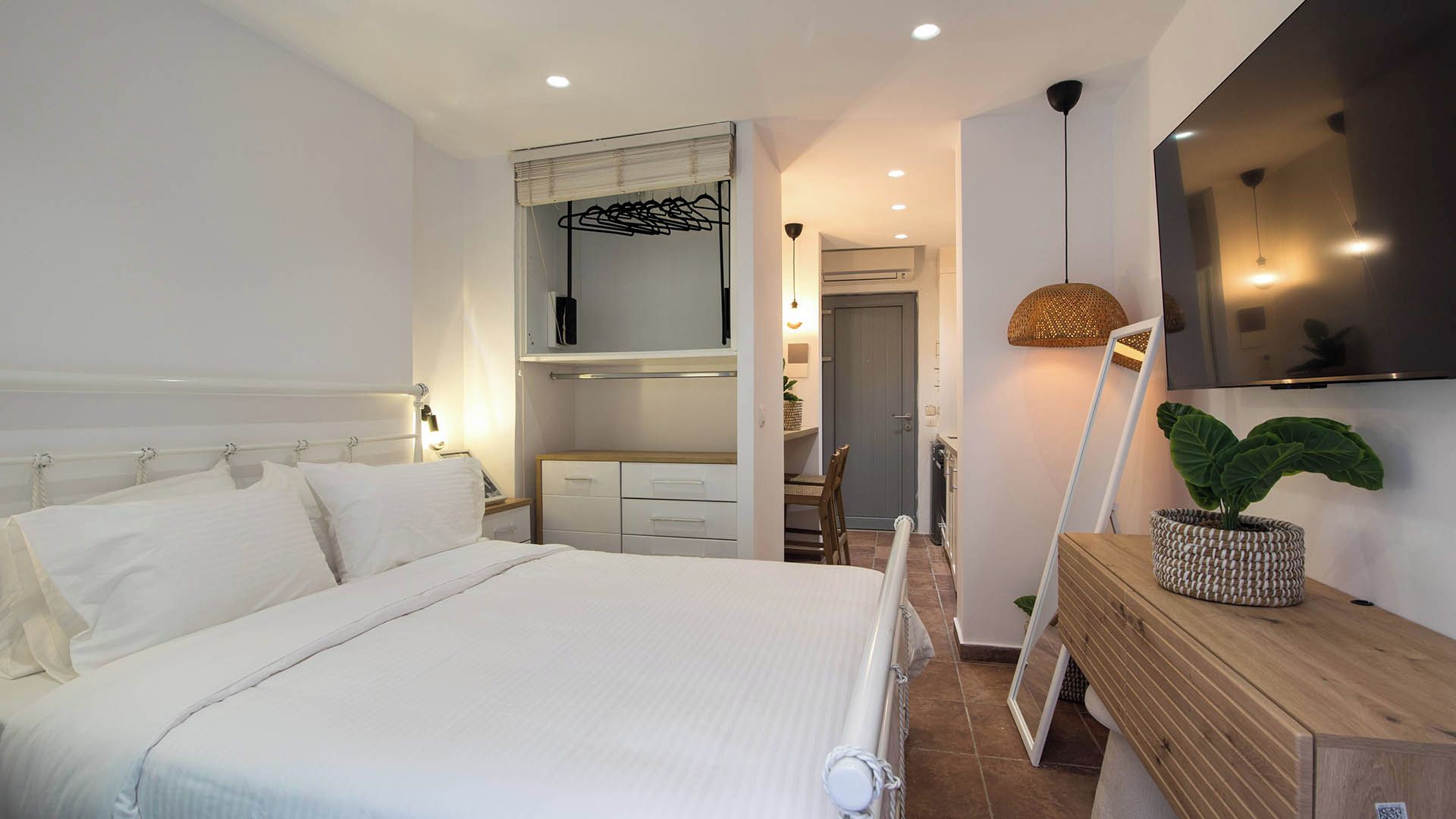 A bedroom with a bed, a bedside table, a TV mounted on the wall, and a door leading to a bathroom.