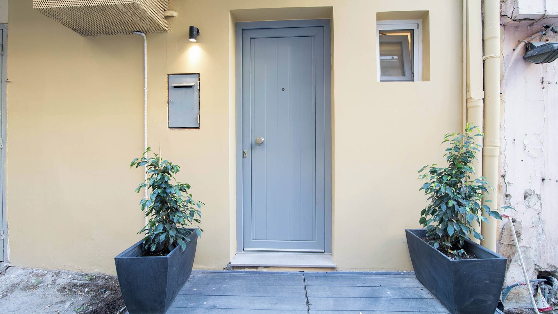 A building entrance with a closed door, a small window, and two potted plants on either side.