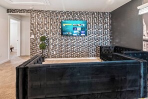 Ein modernes Wohnzimmer mit Wand im Steinoptik, einem Wandfernseher und üppigen schwarzen Sofas.