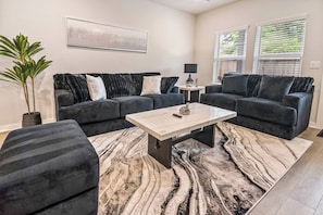 A living room with a sectional sofa, a coffee table, and a patterned rug. - Harry Potter Thematic Bedroom | New York Game Room | Backyard (Magnolia)