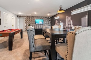 A room with a pool table, dining table, and chairs, a television mounted on a textured wall, and a cityscape mural. - Harry Potter Thematic Bedroom | New York Game Room | Backyard (Magnolia)