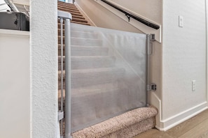A staircase with a carpeted landing and a metal safety gate at the bottom. - Harry Potter Thematic Bedroom | New York Game Room | Backyard (Magnolia)