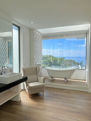 A modern bathroom with a large window, a bathtub, a vanity with a sink, and a chair. - MoonShadow Villa Phuket (Kathu District)
