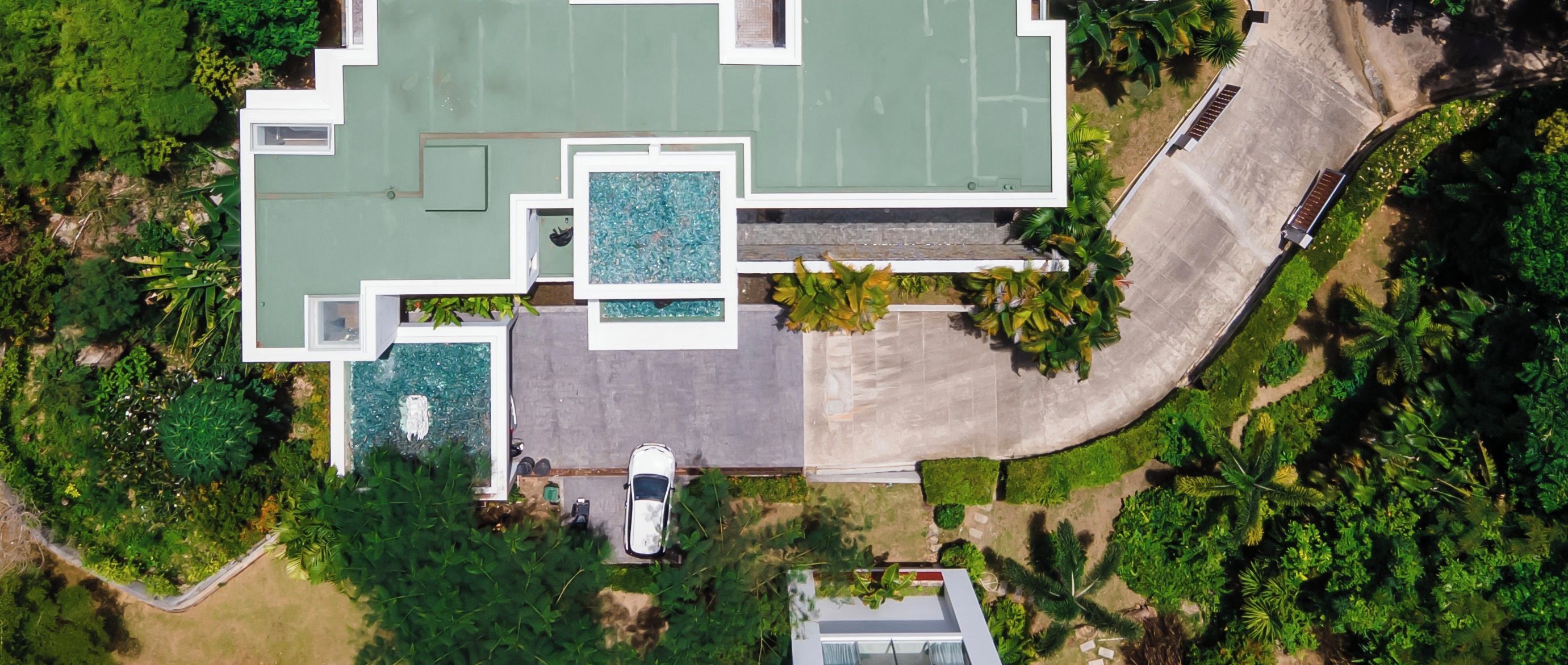 Vista aérea de una casa moderna con piscina, camino de entrada y vegetación circundante.
