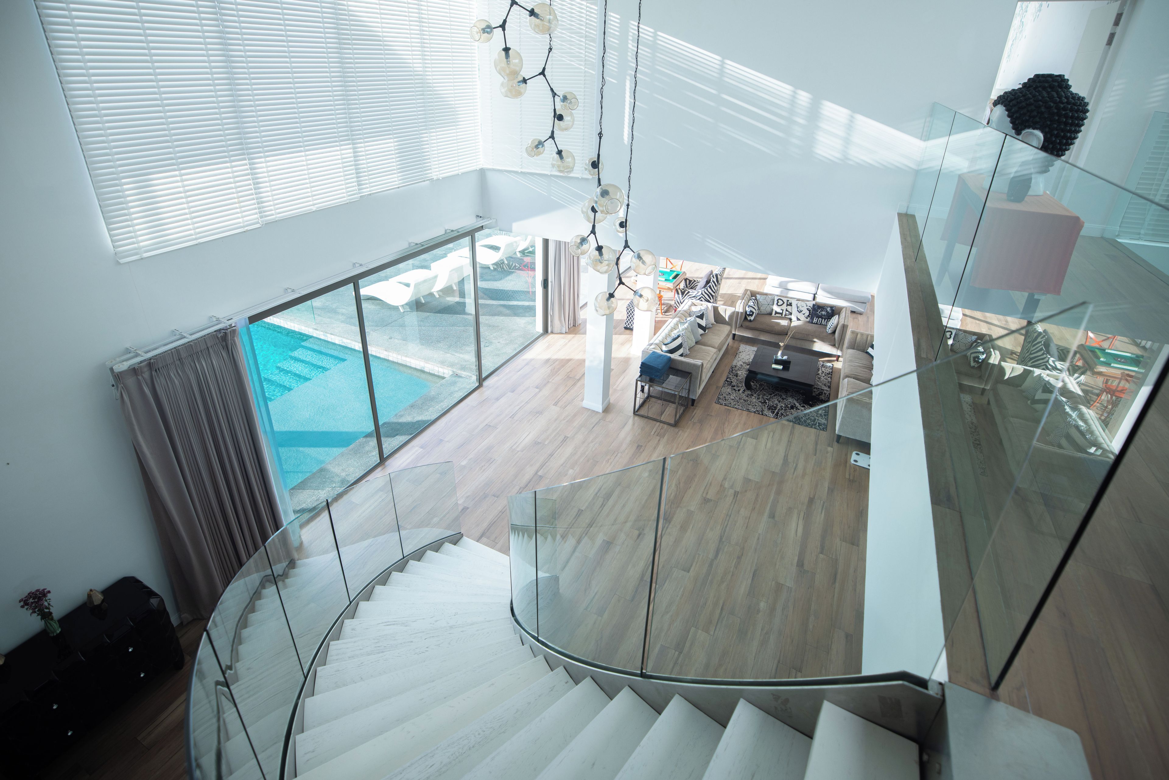 Un interior moderno con una escalera de cristal que lleva a una sala de estar con vista a una piscina.