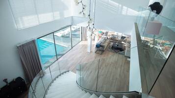 Un interior moderno con una escalera de cristal que lleva a una sala de estar con vista a una piscina.