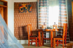A room with a brick wall, a painting of elephants, a table with chairs, and patterned curtains.