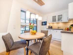 A modern kitchen with white cabinets, a round wooden table, and a fruit bowl. - Holiday Apartment With 1 Bedroom (Zingst)