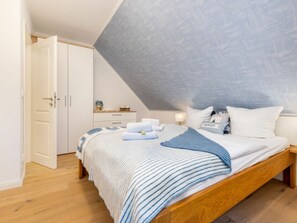A bedroom with a sloped ceiling, a bed with striped bedding, a nightstand, and a dresser. - Holiday Apartment With 1 Bedroom (Zingst)