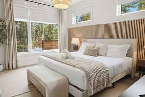 A modern bedroom with a large bed, a wooden headboard, a bedside table with a lamp, and a view of the outdoors. - Muskoka Pines -Private Oasis Spa- Hot Tub & Sauna (Lake of Bays)
