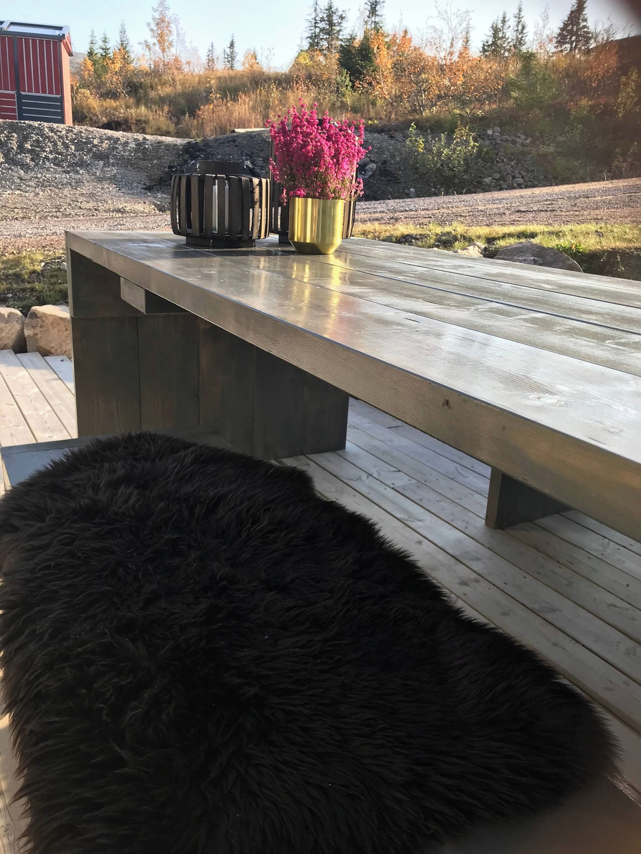 A wooden deck with a bench and a fluffy black ottoman.