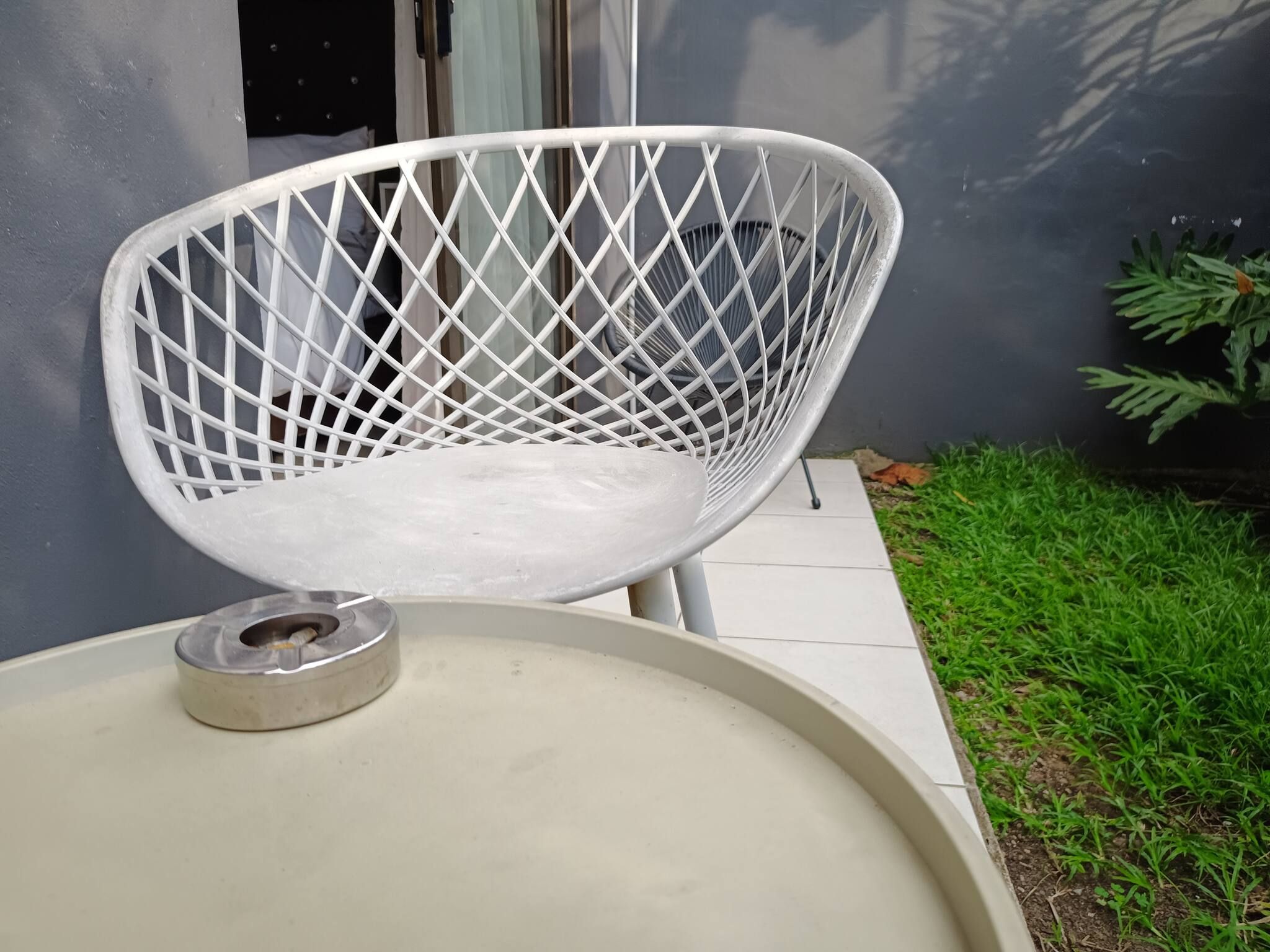 A white chair with a diamond-patterned backrest placed on a white surface, possibly a table or a bench, with a metal object on it.