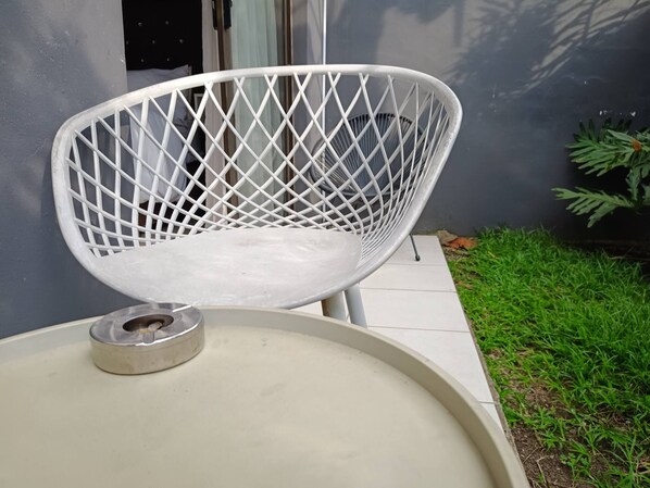 Une chaise blanche avec un dossier orné d’un motif en losanges, placée sur une surface blanche, peut-être une table ou un banc, et sur laquelle se trouve un objet métallique.
