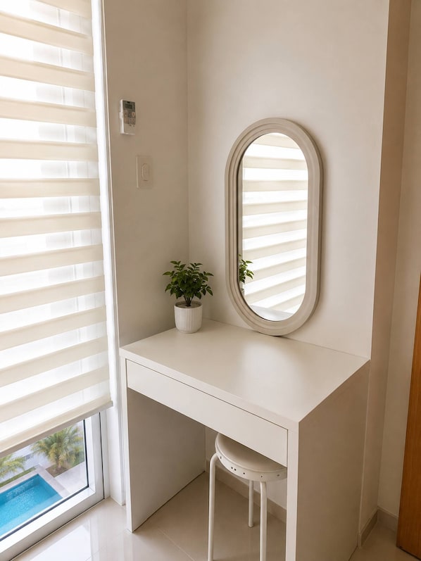 A white desk with a mirror, a potted plant, and a window with blinds. - Quaint 1BR Condo Terrace-pool view MOA-Shell (Pasay City)