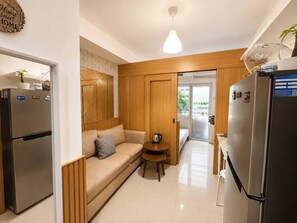 A compact kitchen with a refrigerator, a wooden cabinet, a sofa, and a small table. - Quaint 1BR Condo Terrace-pool view MOA-Shell (Pasay City)