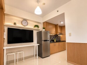 A modern kitchen with a built-in refrigerator, a flat-screen TV, wooden cabinets, and a tiled floor. - Quaint 1BR Condo Terrace-pool view MOA-Shell (Pasay City)