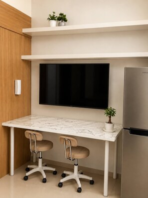 A modern kitchen with a marble countertop, two office chairs, a flat-screen TV, a stainless steel refrigerator, and two potted plants on a shelf. - Quaint 1BR Condo Terrace-pool view MOA-Shell (Pasay City)