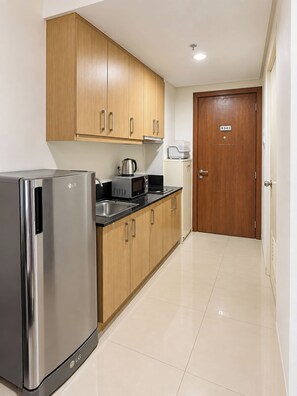 A modern kitchen with stainless steel appliances, wooden cabinets, and a tiled floor. - Zen Escape 1Br with Balcony pacing pool (Pasay City)
