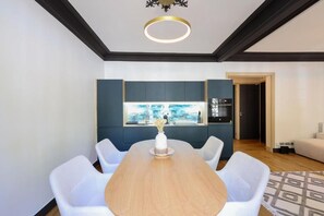 Ein moderner Essbereich mit Holztisch und weißen Stühlen, eine Küche mit dunklen Schränken und Blick durch ein Fenster.