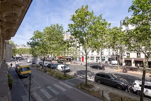 Straßenansicht mit parkenden Autos, Bäumen entlang der Straße und Gebäuden im Hintergrund.
