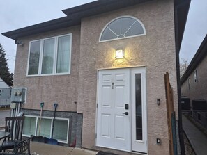 A two-story house with a large front door, a garage door, and a covered patio area. - D-King's Royal Court (Regina)