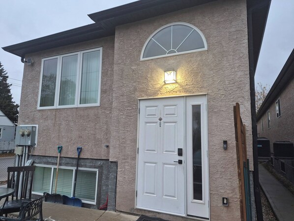 A two-story house with a large front door, a garage door, and a covered patio area. - D-King's Royal Court (Regina)