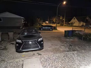 A residential driveway at night with a black SUV parked in the foreground. - D-King's Royal Court (Regina)