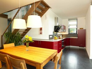 Eine moderne Küche mit roten Schränken, einem Holztisch und einer Treppe mit Holzbalken.