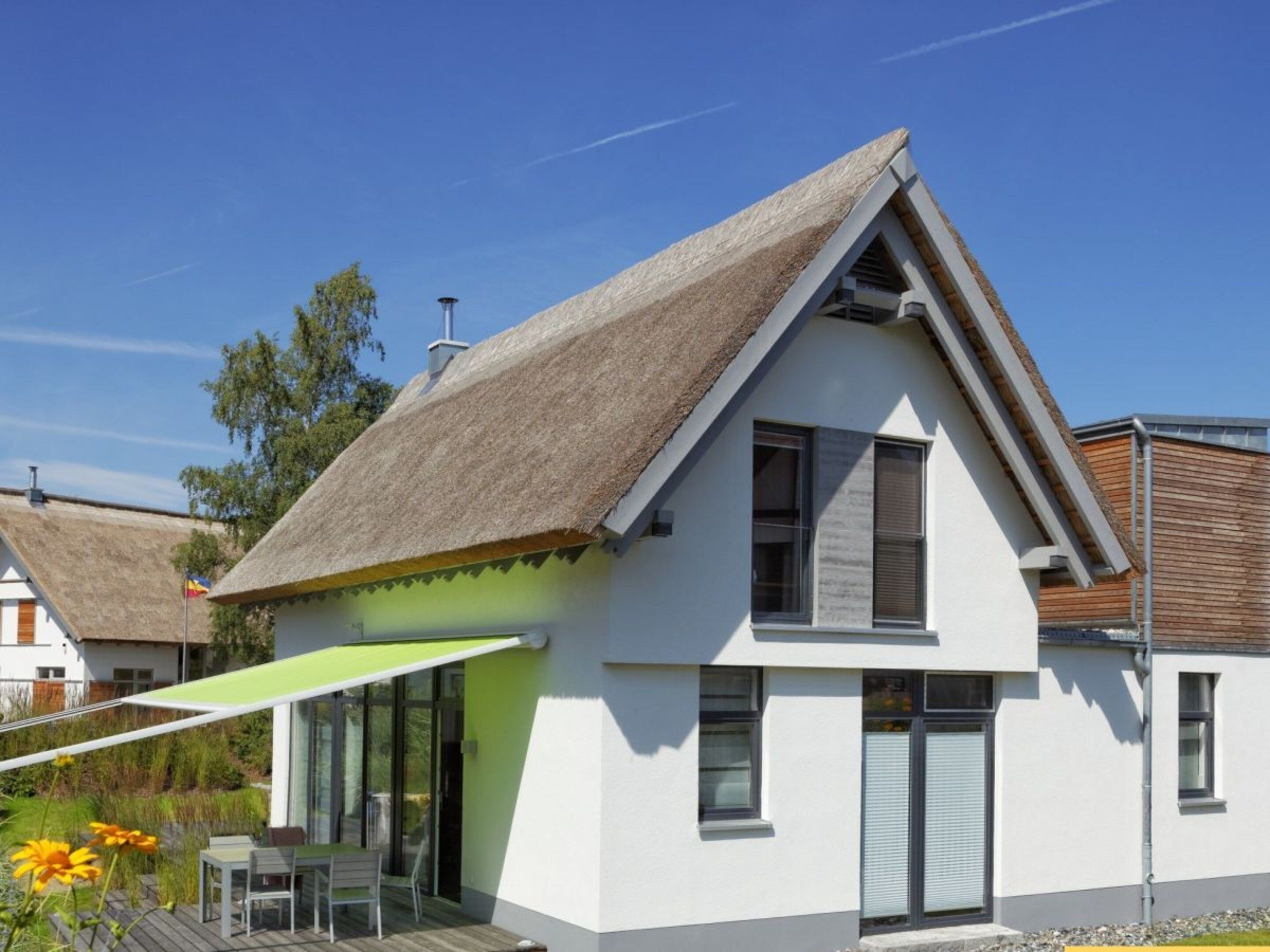 Ein modernes Haus mit Satteldach, einer Terrasse mit Tisch und Stühlen und einem strahlend blauen Himmel.