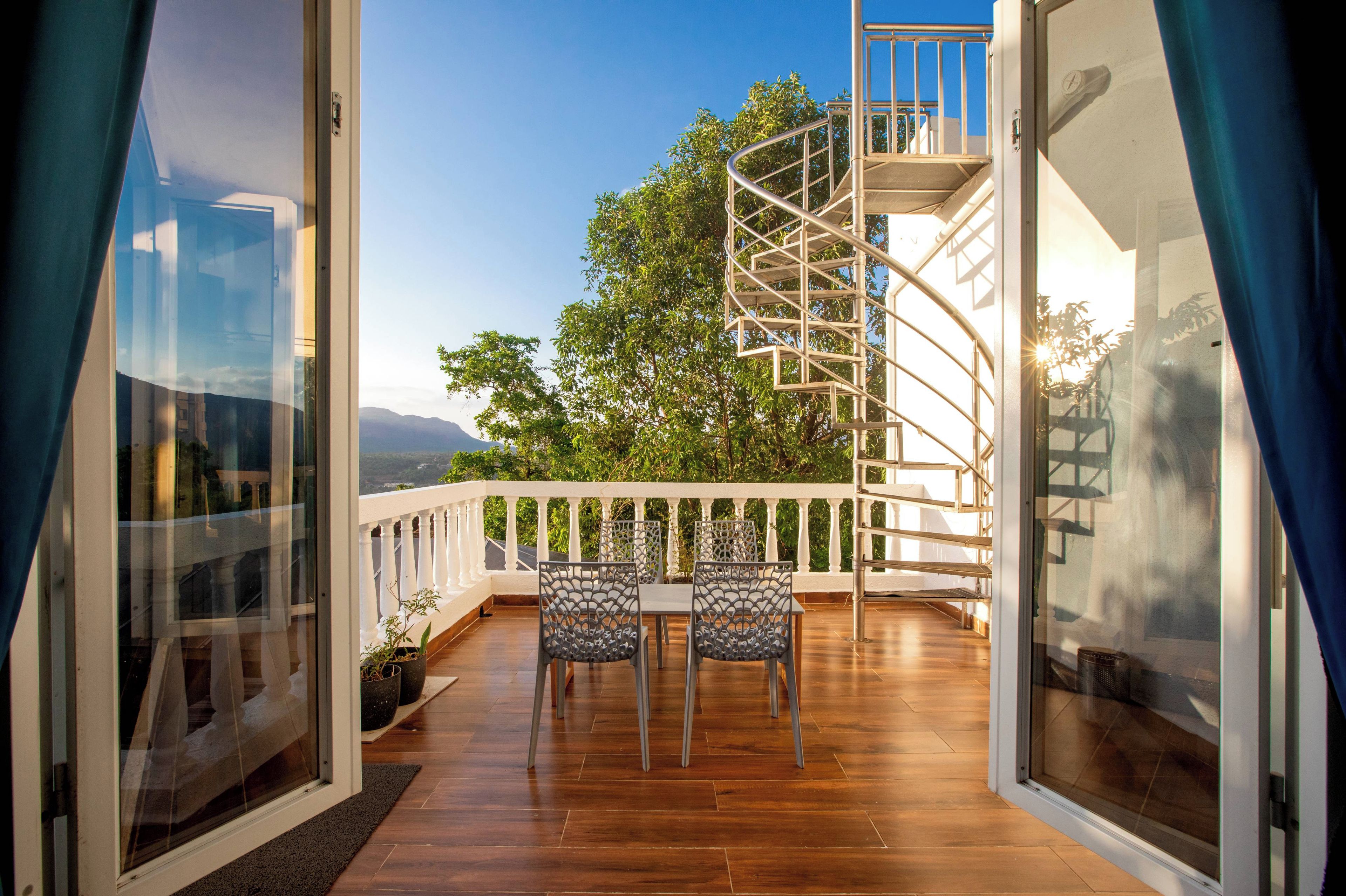 A balcony with a spiral staircase, wooden flooring, and two chairs.