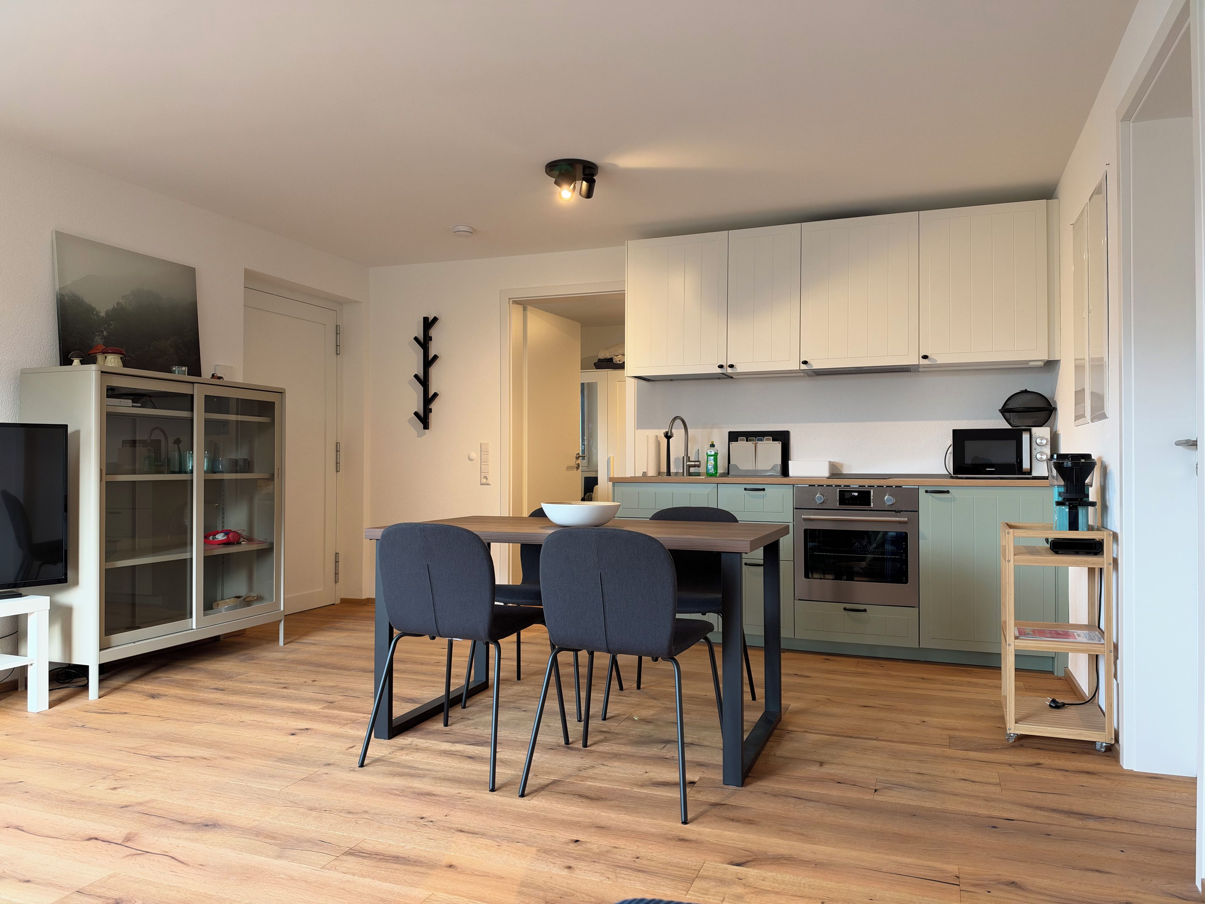 Une cuisine moderne avec des meubles blancs, une table à manger avec des chaises et un plancher en bois.