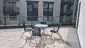 Ein Balkon mit Tisch und Stühlen, einer Glasufernung und einem Gebäude im Hintergrund.