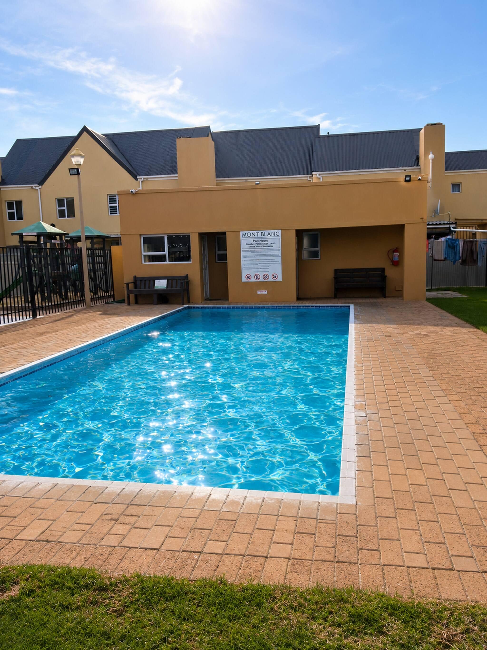 A swimming pool with a brick border, a signboard, and a fenced play area.