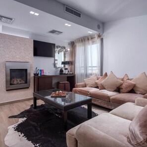 A modern living room with a fireplace, a sofa set, a coffee table, and a flat-screen TV mounted on the wall. - Habitat Hotel Kilkis (Kilkis)