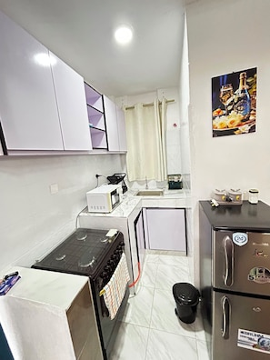 A compact kitchen with a stove, microwave, sink, and refrigerator. - Cozy 1-bedroom apartment with AC in wonderful Nairobi with JKIA and Park (Nairobi)