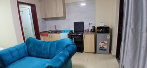 A compact living space with a kitchenette, a blue sofa, and a refrigerator. - Cozy 1-bedroom apartment with AC in wonderful Nairobi with JKIA and Park (Nairobi)